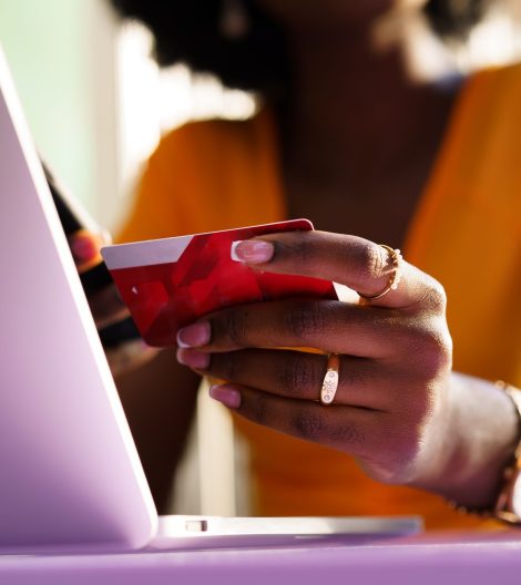 Happy young african woman holding credit card while shopping via laptop sitting in outdoor cafe, close up